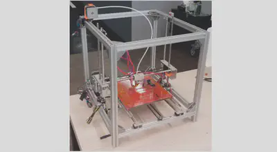 Image of the Metal Reviser 3D printer on a desk. The frame is mainly made of aluminum frames.