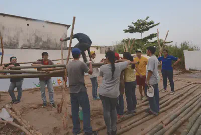 Group a students gathered around the bamboo structure. A student climbing on top of it to test if it could hold his weight.