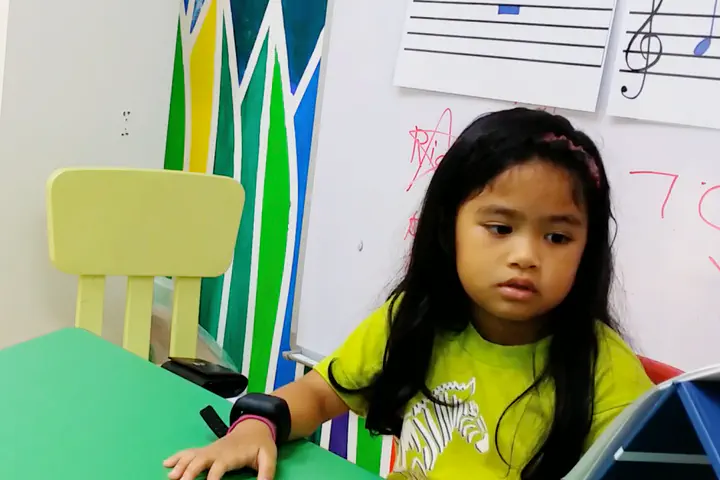 Child seated by a table in kindergarten, wearing wristband with physiological sensors