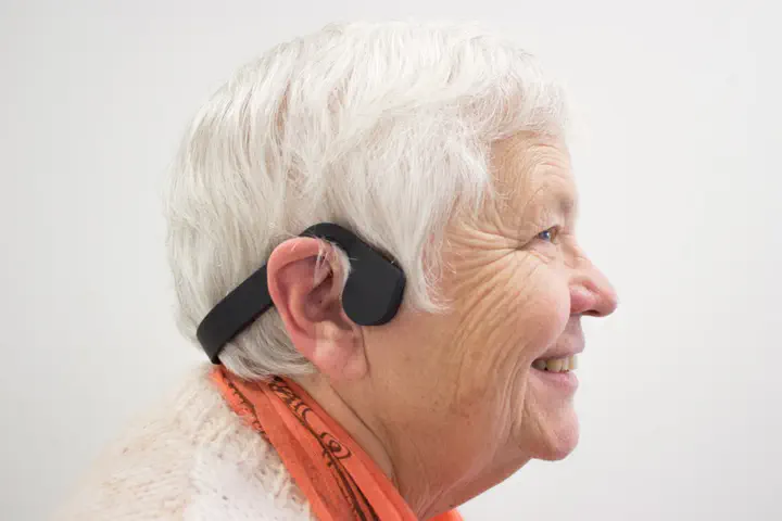 Older adult wearing bone-conduction headset connected to Prompto