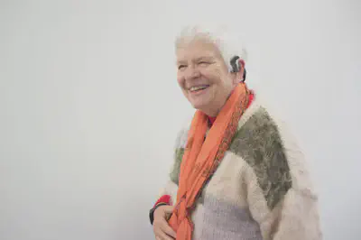 Older adult lady user smiling. She is wearing the E4 wristband and the bone conduction headset. 