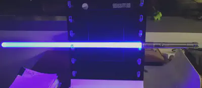 Image of a fully-lit saber with blue-coloured lighting. The saber is placed length-wise on an acrylic stand.
